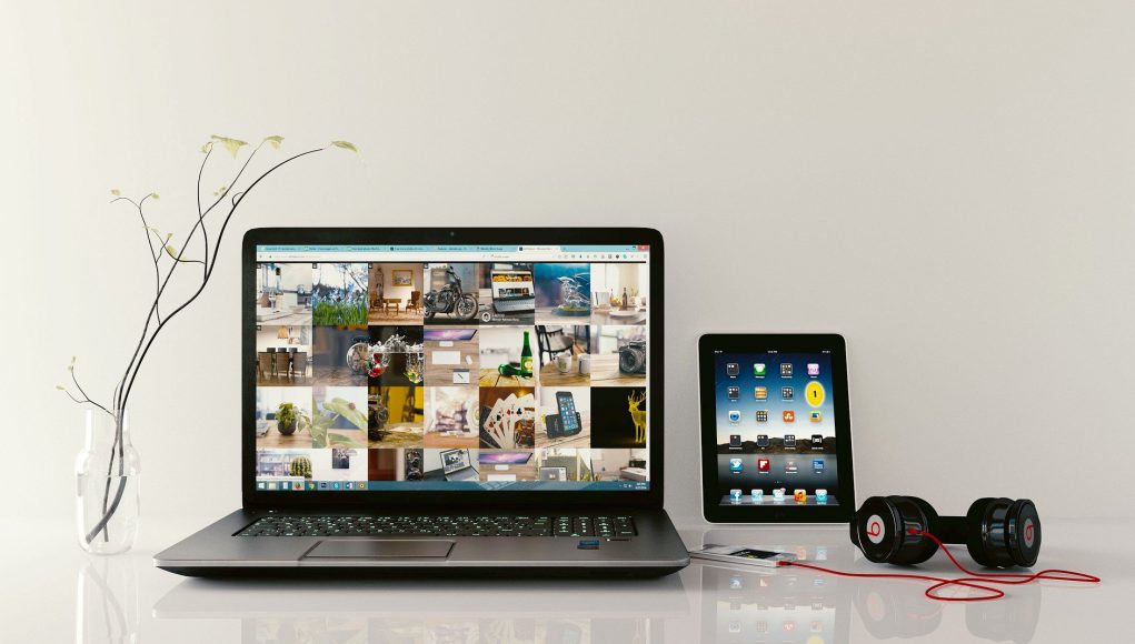 Laptop z wynajmu laptopów biznesowych leży na stole wraz z tabletem, słuchawkami i wazonem.