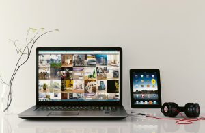 Laptop z wynajmu laptopów biznesowych leży na stole wraz z tabletem, słuchawkami i wazonem.
