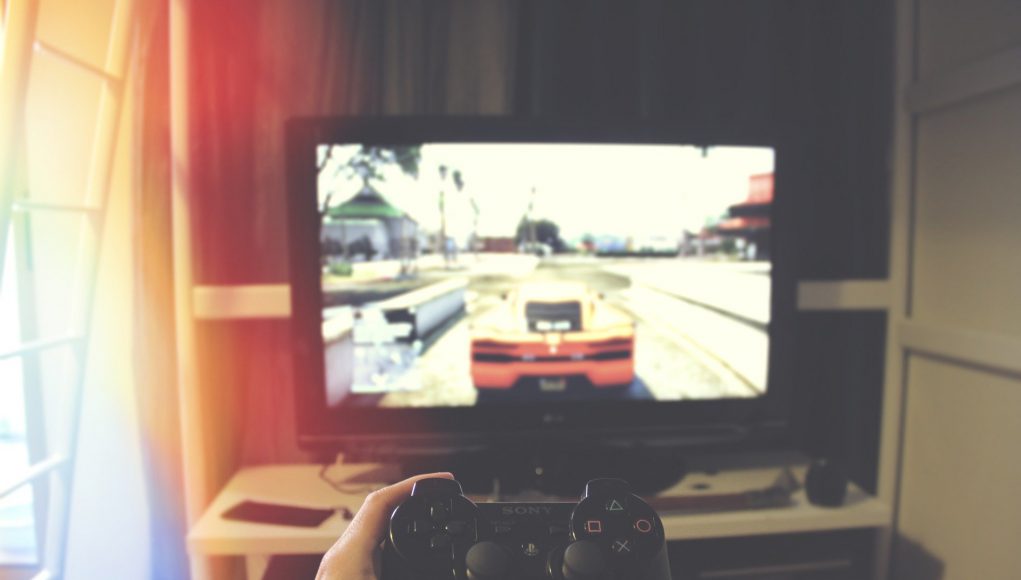 Człowiek grający na konsoli, na ekranie widać rozgrywkę; ujęcie z pierwszej osoby; w ręku jest kontroler